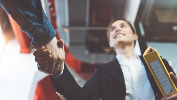 Two people shake hands. One is holding a folder.