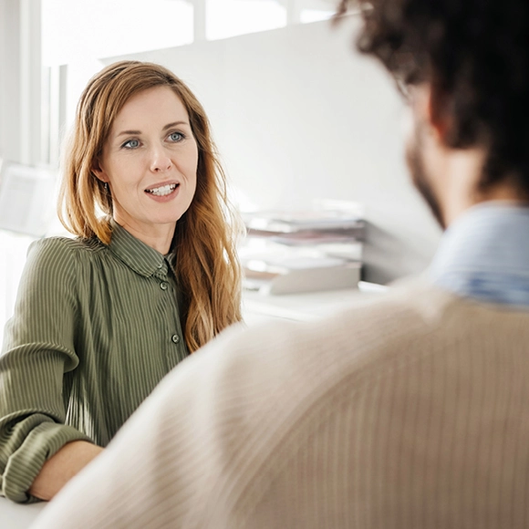 Women with red hair sitting at a desk talking to another person